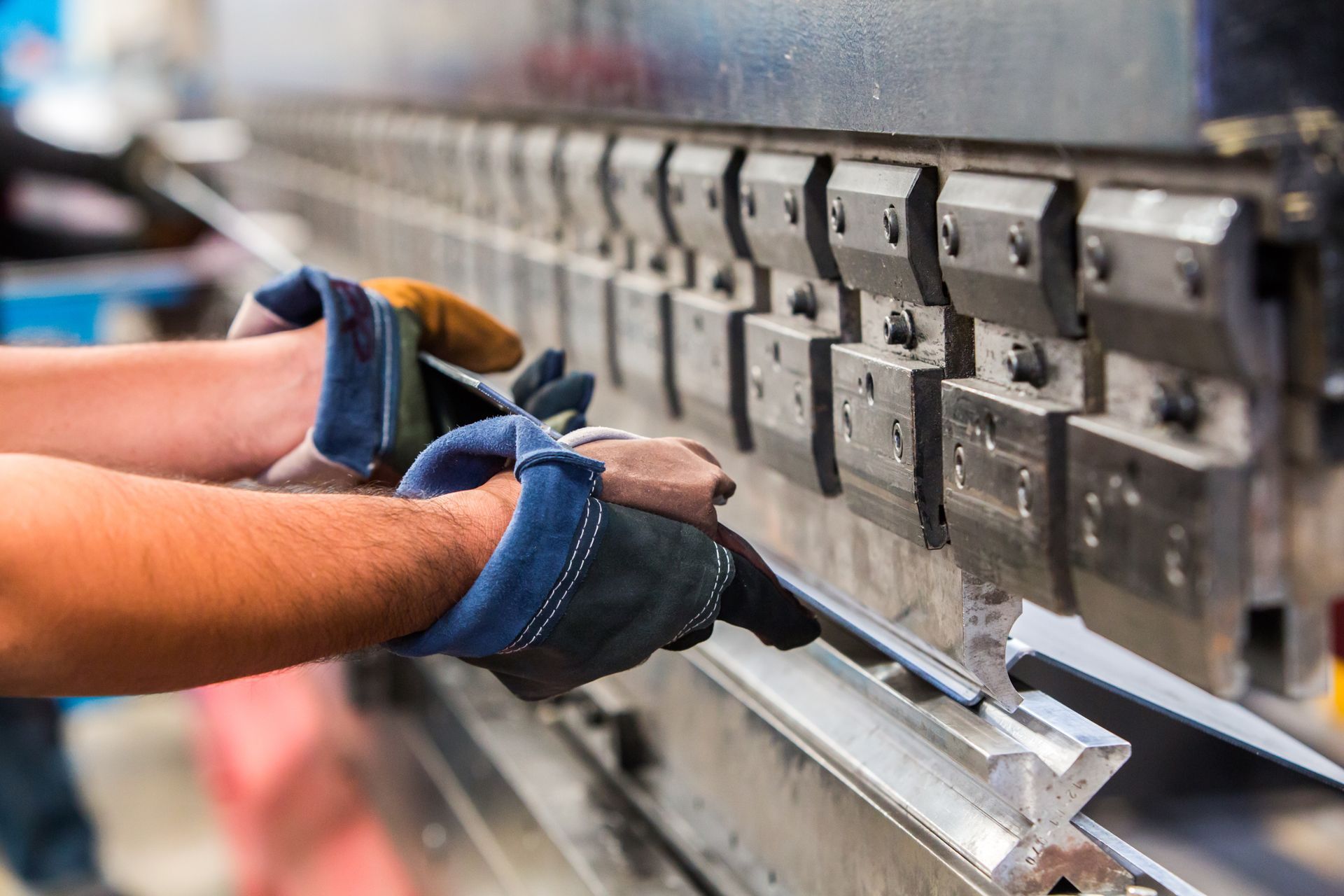 Hands wearing gloves bending metal sheet with a metal brake machine.