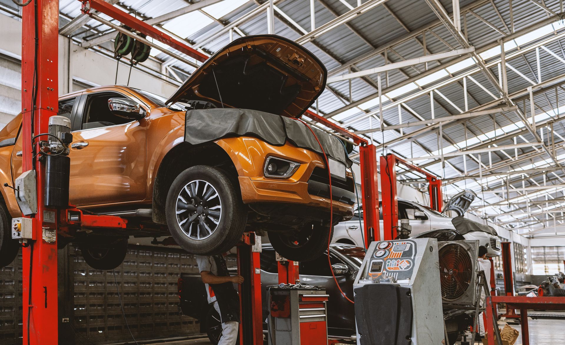 Orange truck on a lift in a repair shop with its hood open.
