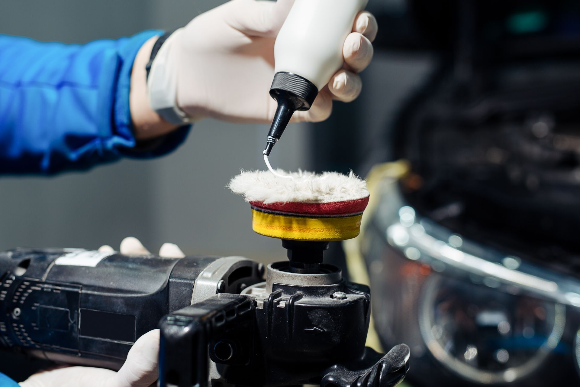 A person in gloves applies polish to a car buffer in a garage.