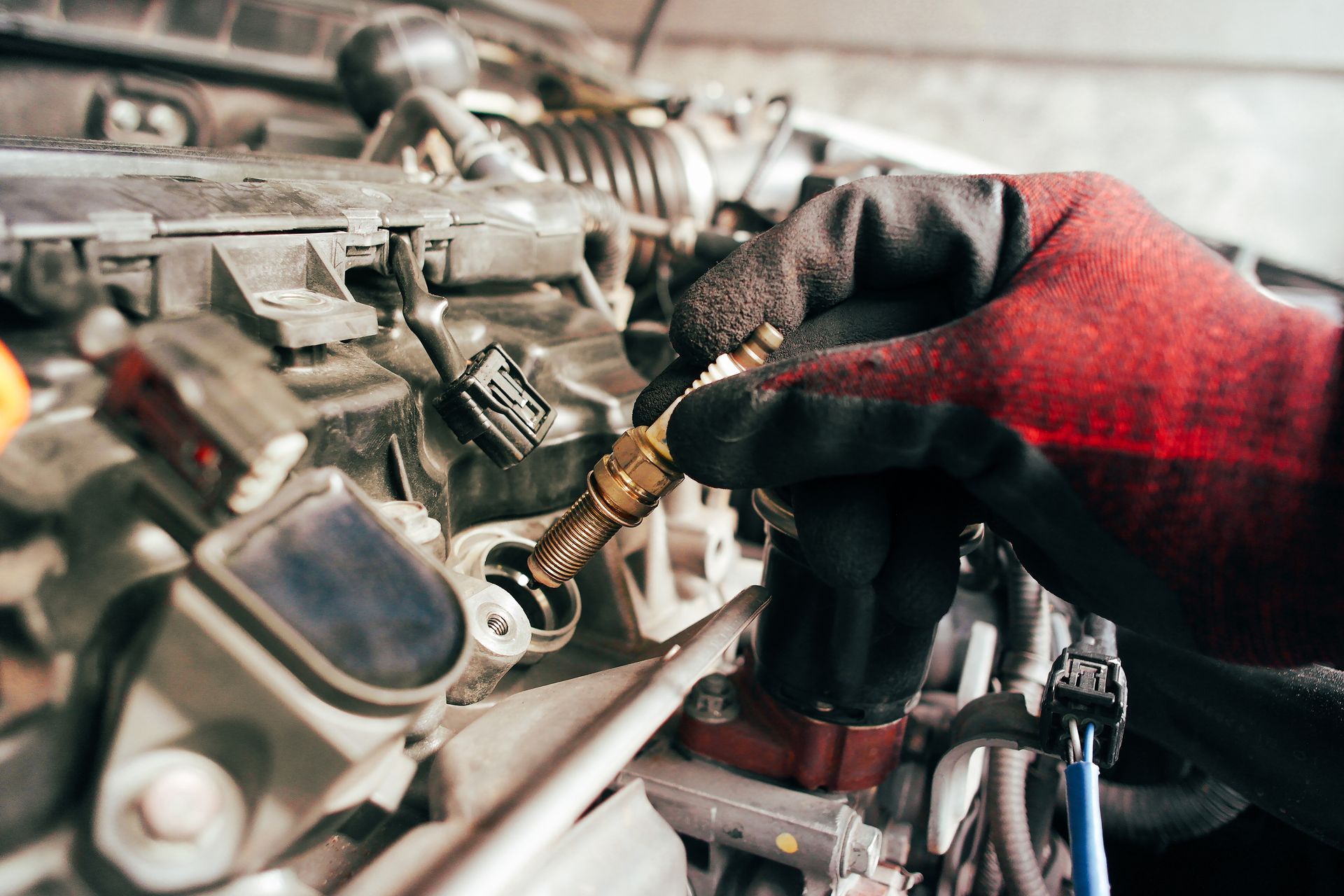 Gloved hand installing spark plug in a car engine.