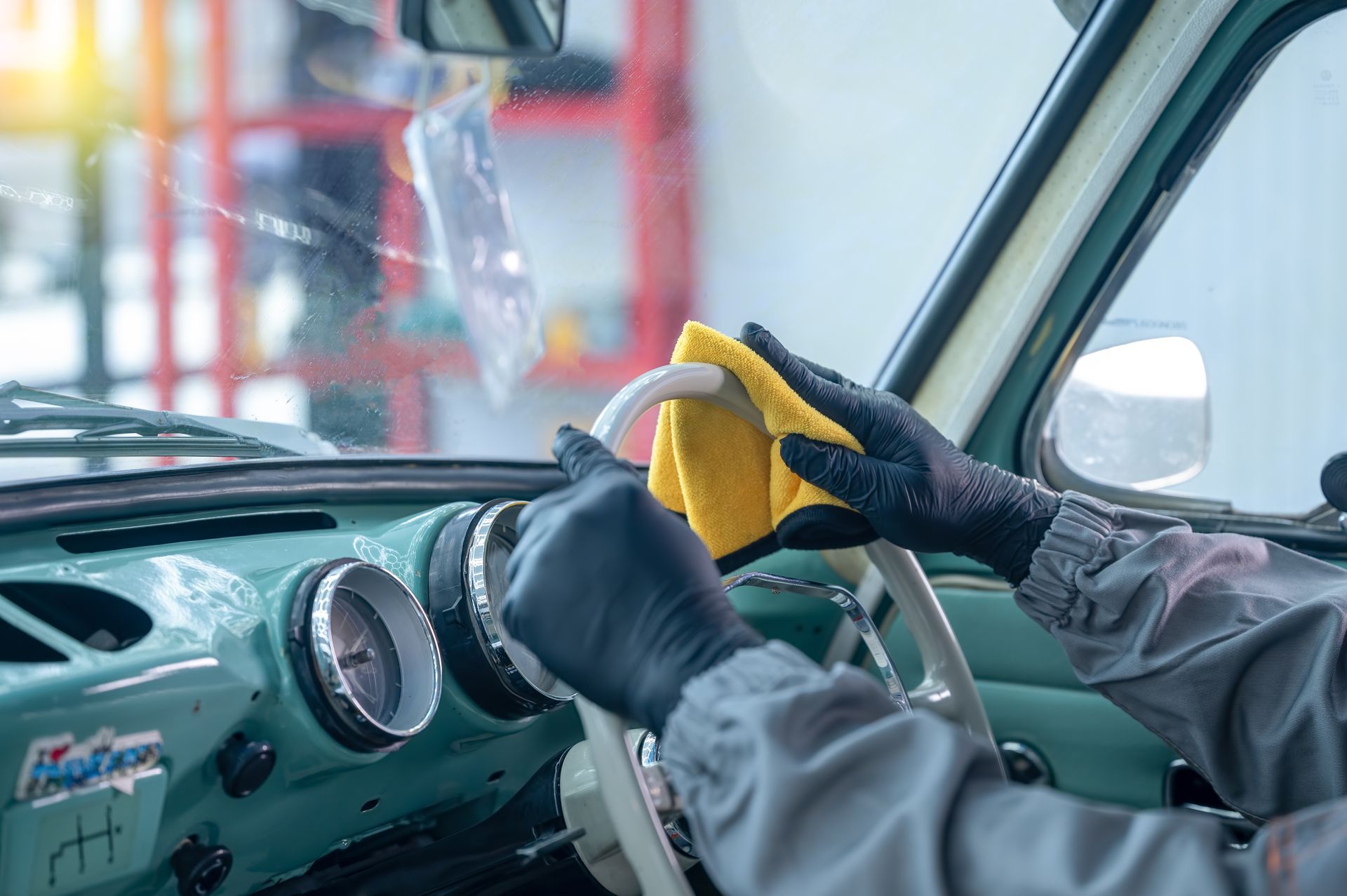 Hands in black gloves cleaning a classic car's interior with a yellow cloth.