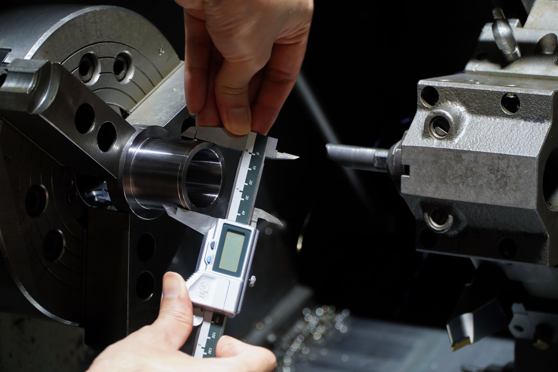 Person using digital calipers to measure a metal component in a lathe.