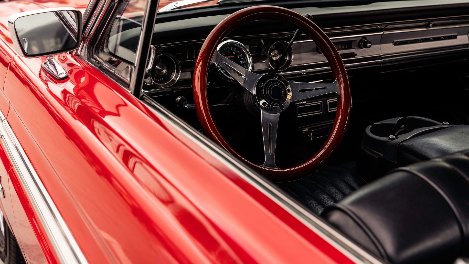 Red classic car interior with a wooden steering wheel.