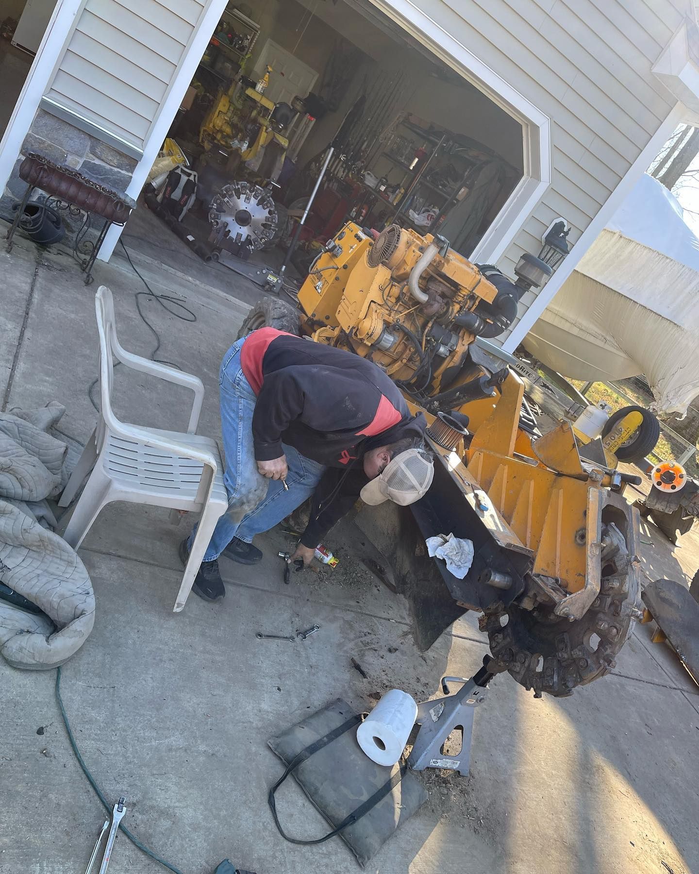 A man is working on a tractor in front of a garage.