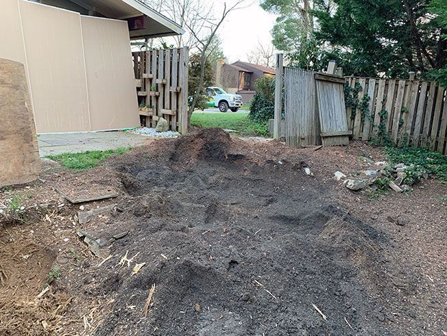 A pile of dirt in a backyard next to a wooden fence.