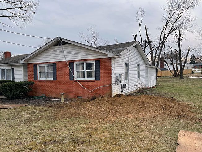 A small brick and white house with a dug-up yard and bare trees under an overcast sky.