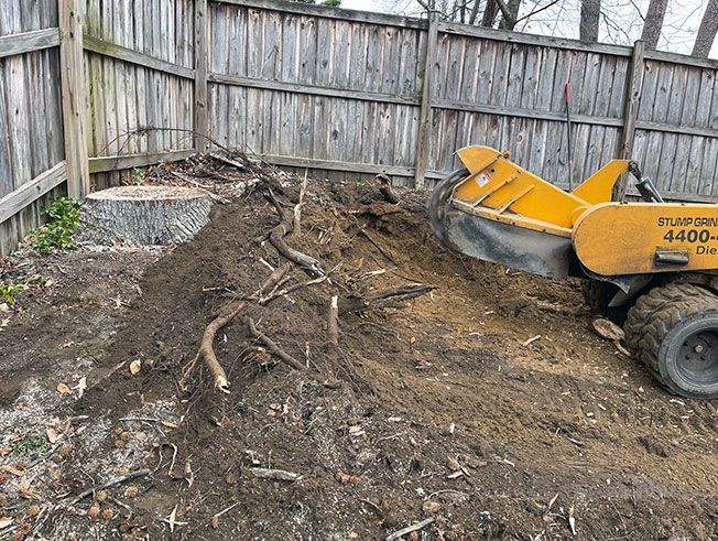 A stump grinder is sitting in the dirt next to a wooden fence.