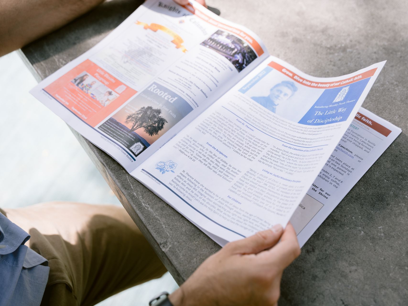 Person reading an open magazine outdoors on a stone ledge