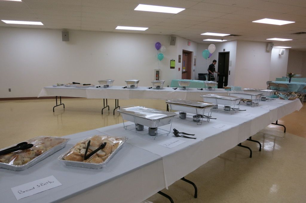 Long banquet table with trays of food in a bright, empty room