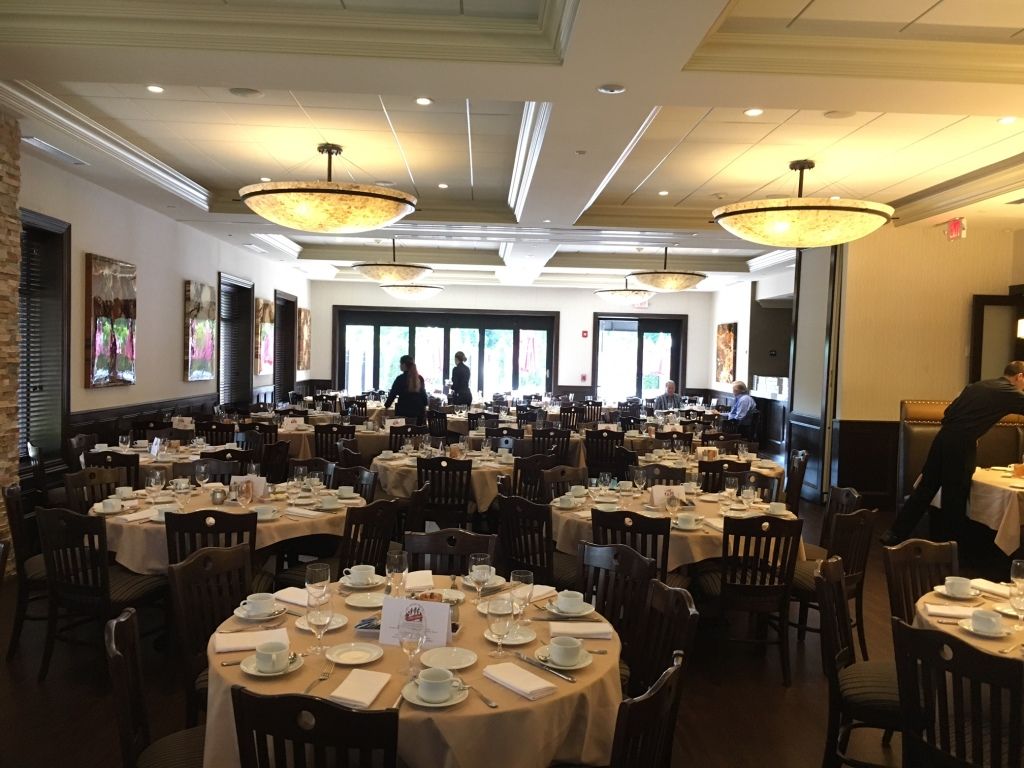 Elegant banquet hall with round tables, white tablecloths, and chandeliers near a bright entrance.