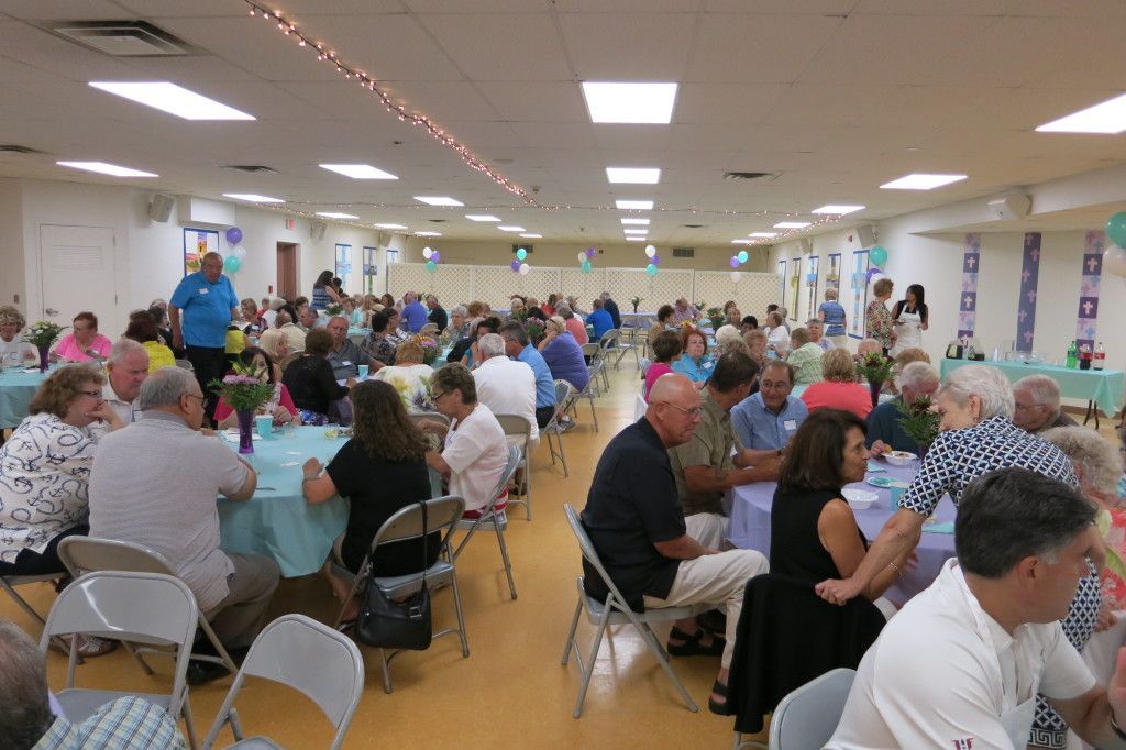 Large community hall filled with people seated at round tables during a social gathering