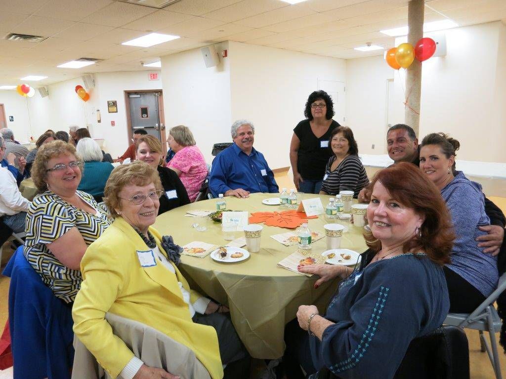 People seated around a round table at a decorated indoor gathering, smiling and eating together.