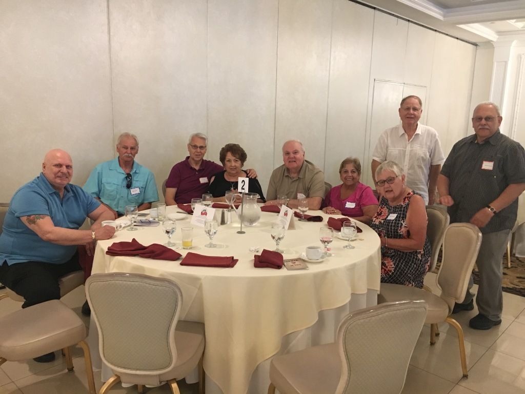 Group gathered around a banquet table in a bright dining room, smiling for a meal or celebration.