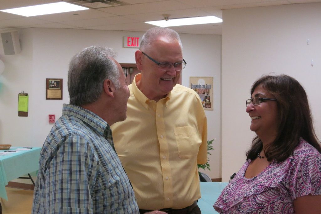 Three people chatting in a bright indoor room, smiling and facing each other.