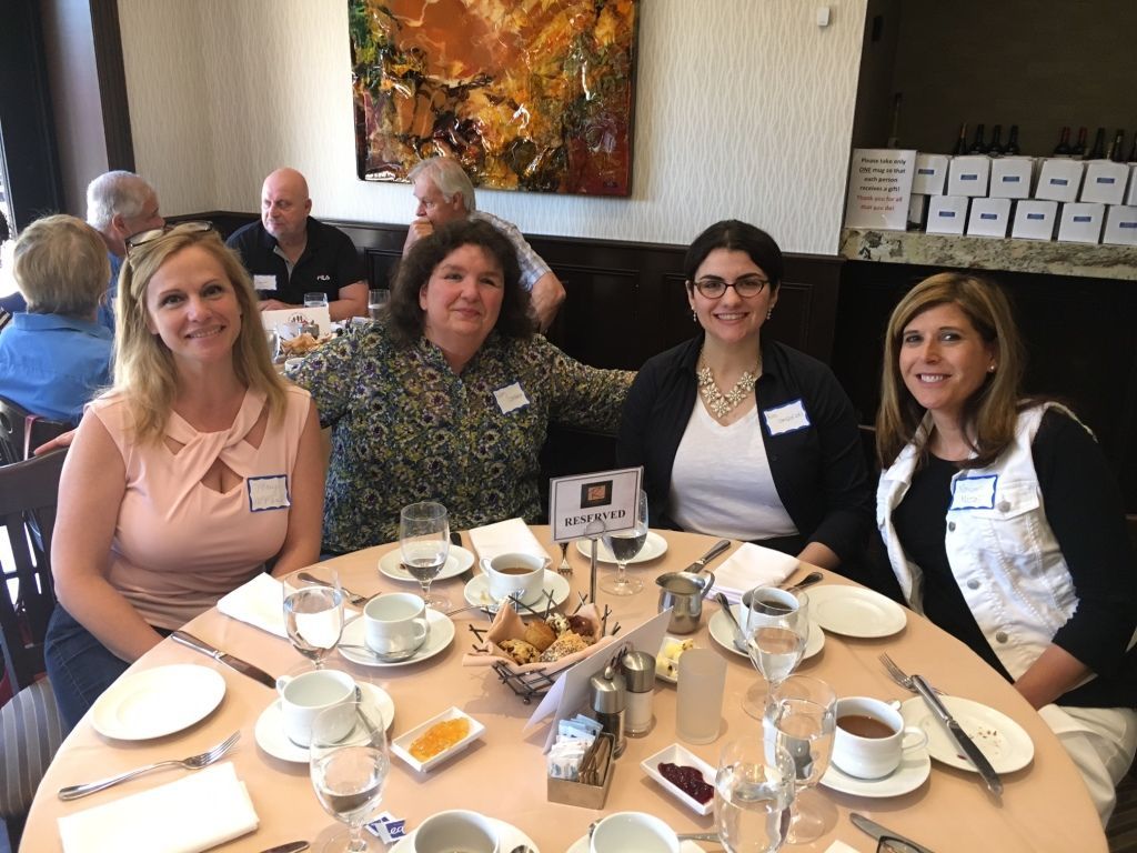 Four people smiling at a table in a restaurant, with coffee cups and plates set for breakfast