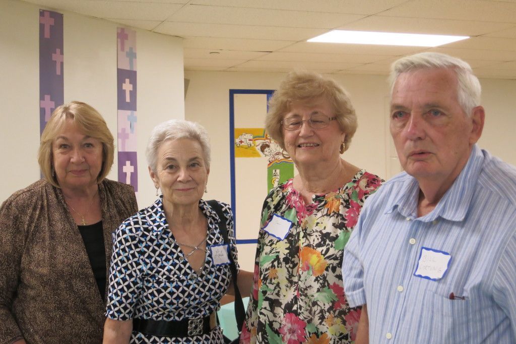 Four people standing together in a hallway, smiling at the camera.