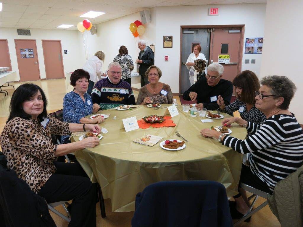 People seated around a banquet table at a community gathering, with food and drinks in a room.