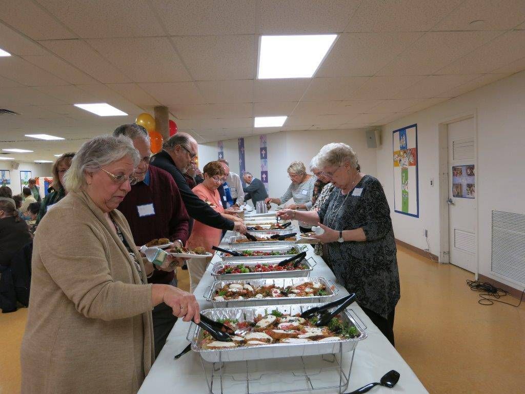 People serving and lining up for food at a buffet in a bright community hall