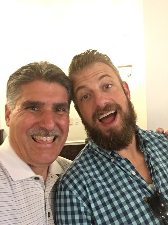 Two smiling people posing closely together indoors, one in a white shirt and one in a blue plaid shirt.