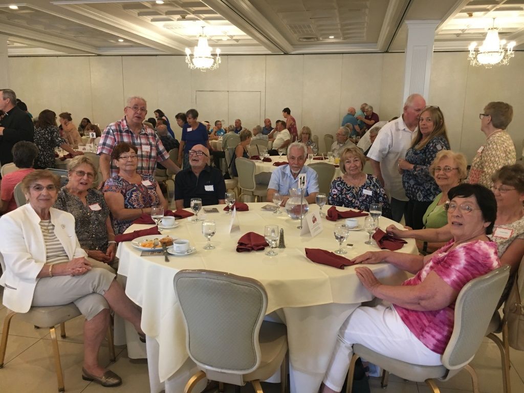 People seated and standing around tables at a banquet in a bright dining hall