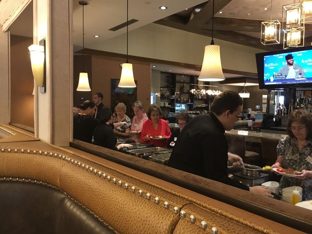 Restaurant diners seated at a counter under warm pendant lights, with a TV visible in the background.