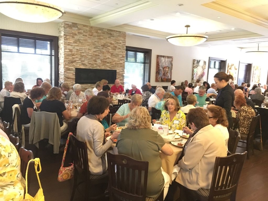 People seated around banquet tables in a bright dining room, chatting during a meal