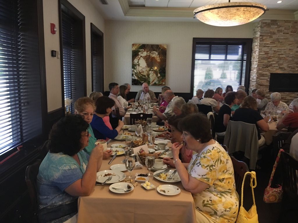 People dining together in a bright restaurant with a long table, plates, drinks, and stone wall decor.