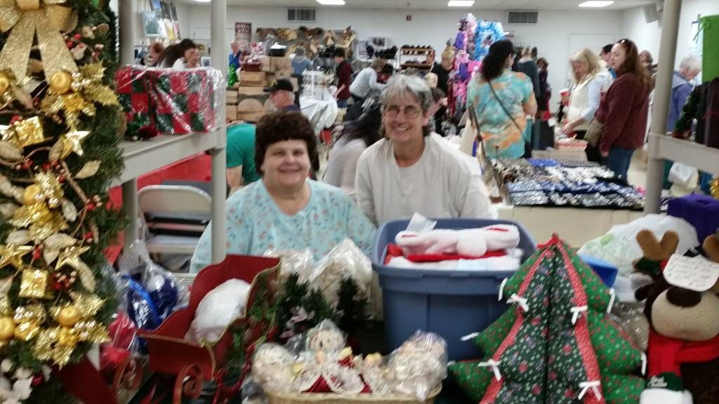 Holiday craft market booth with two people behind tables of Christmas decorations and gifts