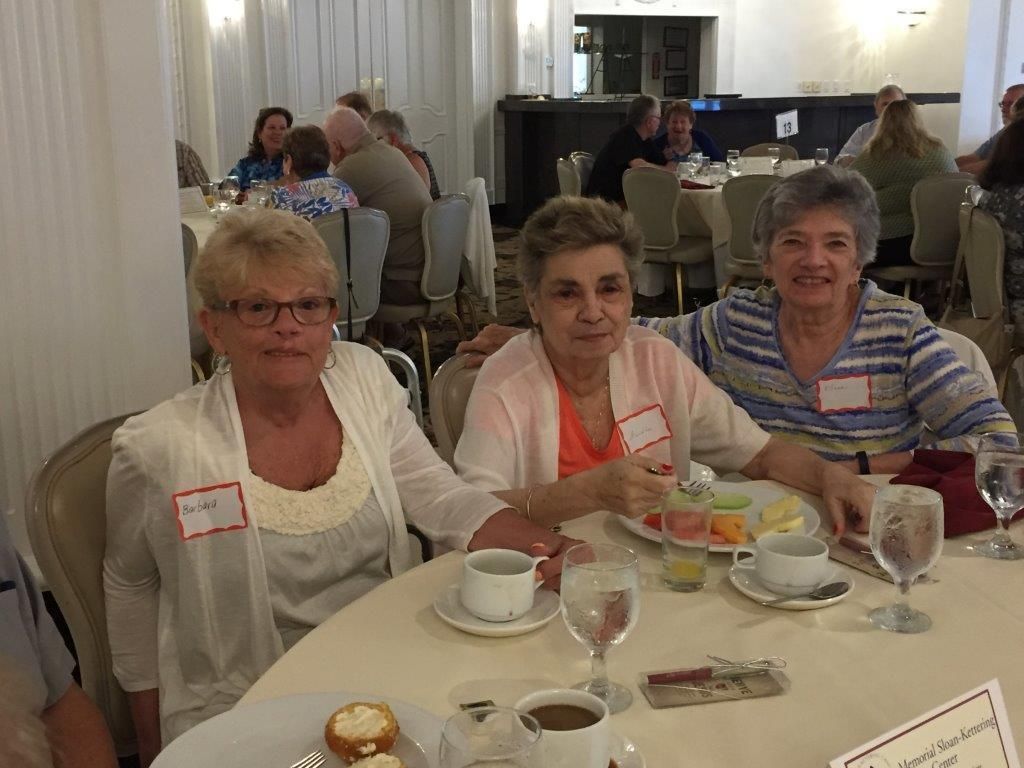 Three women seated at a banquet table with coffee cups and desserts in a restaurant hall