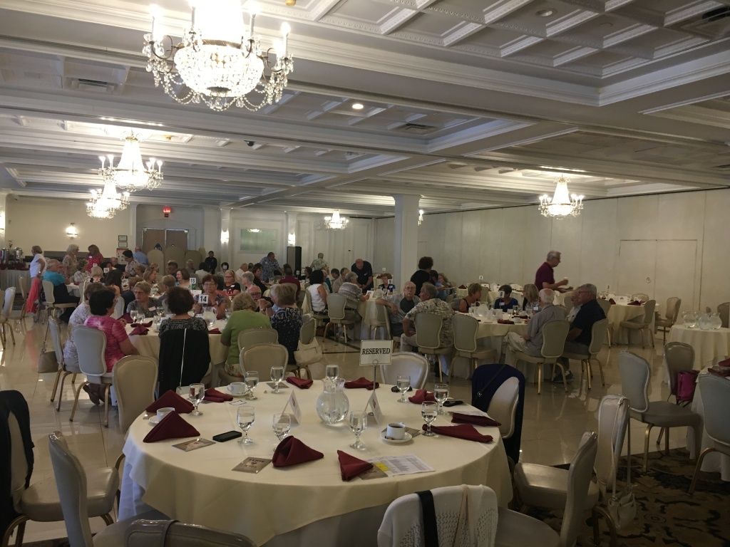 Banquet hall with round tables set for a formal event and many guests seated under chandeliers.