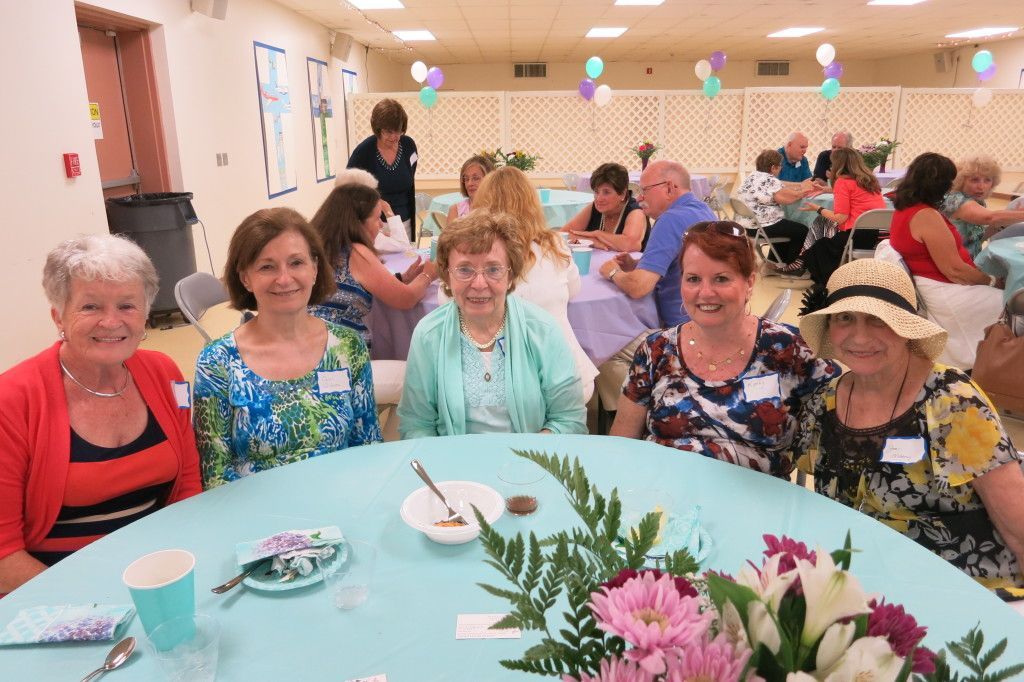 People seated around a long table at a cheerful indoor party with flowers and balloons