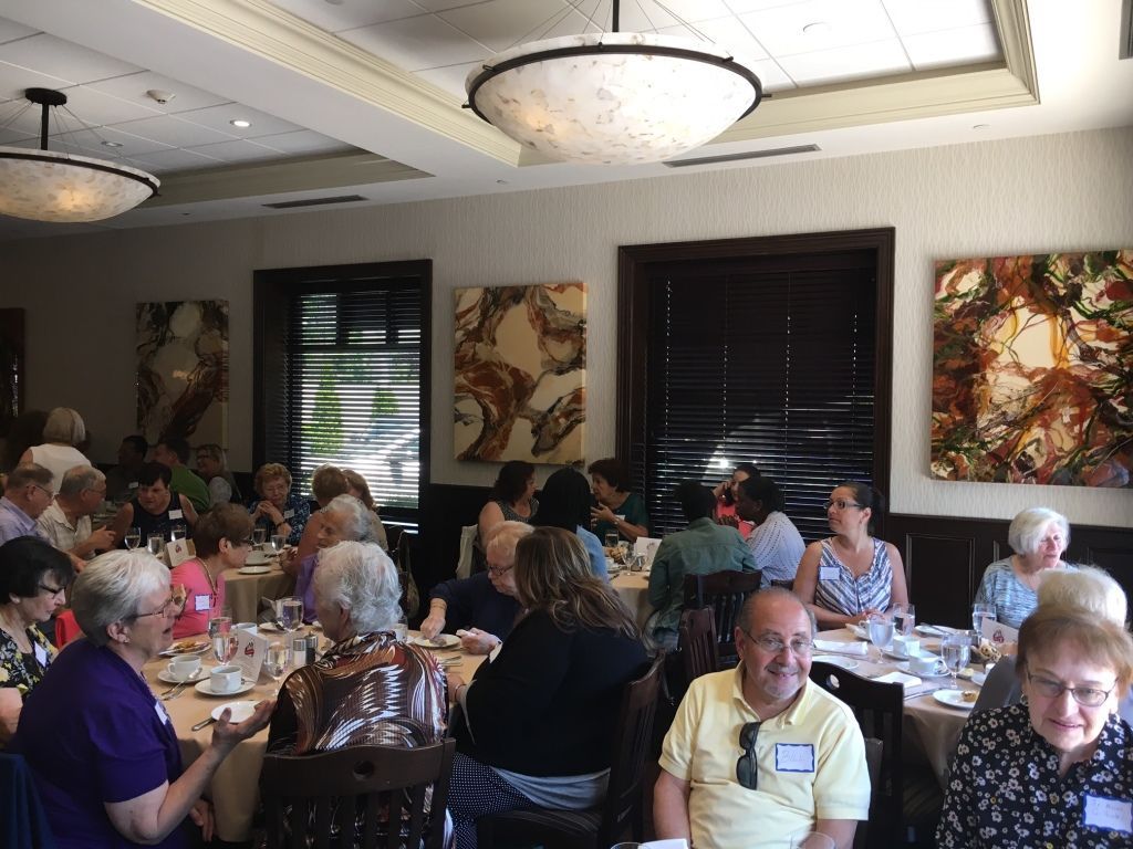 People seated at round tables in a bright banquet room with artwork and chandeliers.