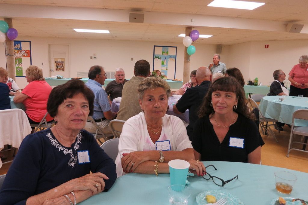 People seated at a table in a community hall, chatting over drinks and snacks.