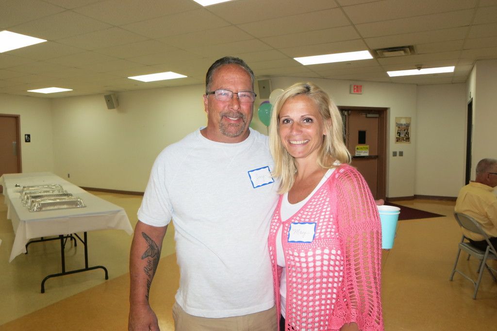 Two people smiling in a meeting room, standing beside tables and folding chairs