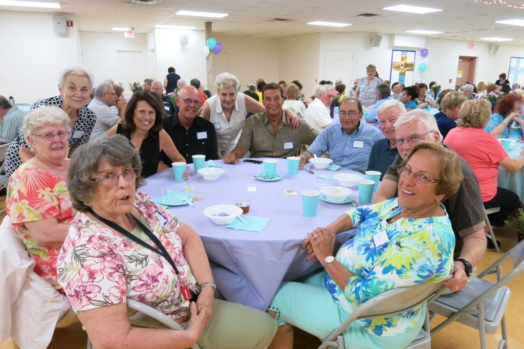 People seated at round tables in a bright community hall, chatting at a social event