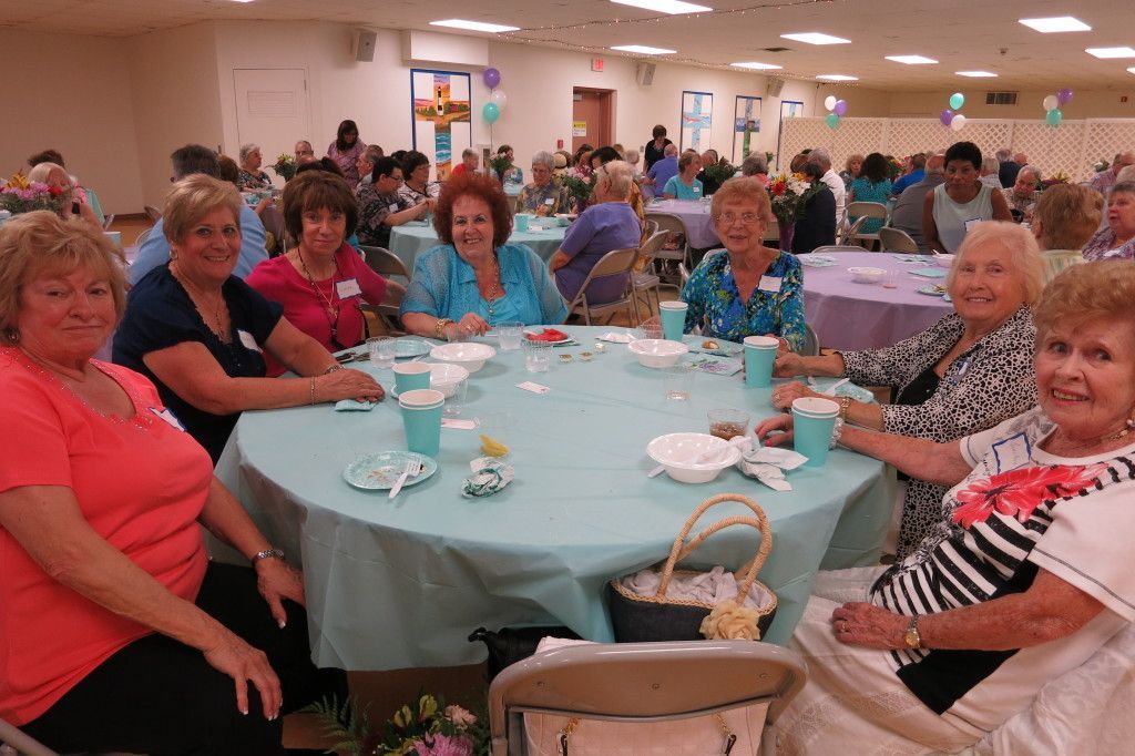 Guests seated at a banquet table in a decorated hall, smiling and chatting at a social event