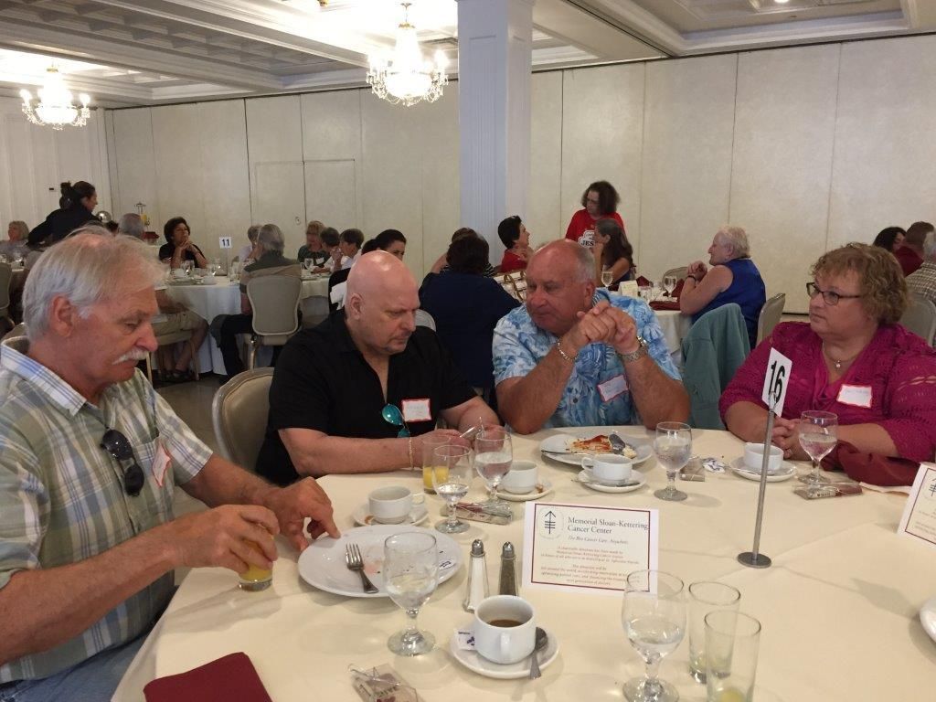 People seated at round tables in a banquet hall, eating and talking during a social event.
