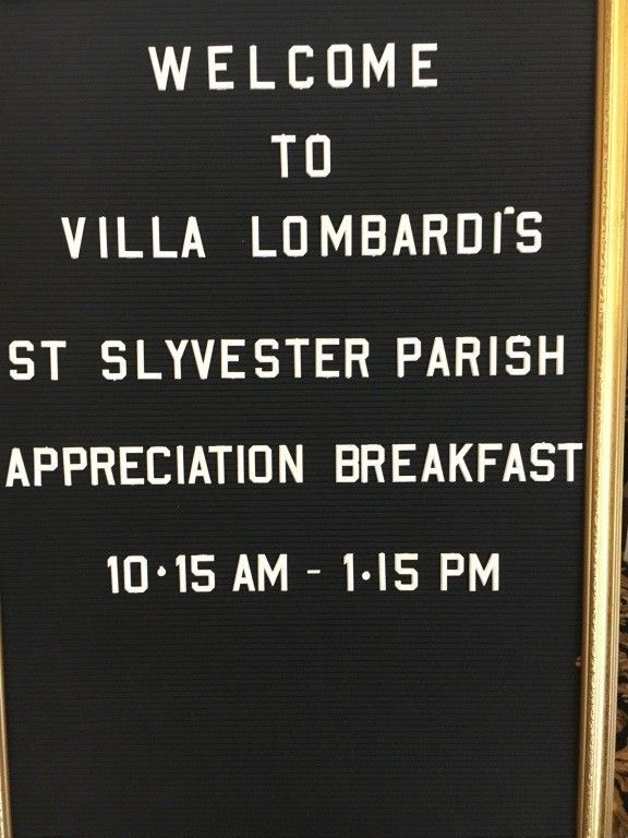 Black sign reads: “Welcome to Villa Lombardi’s St Sylvester Parish Appreciation Breakfast 10:15 AM - 1:15 PM”
