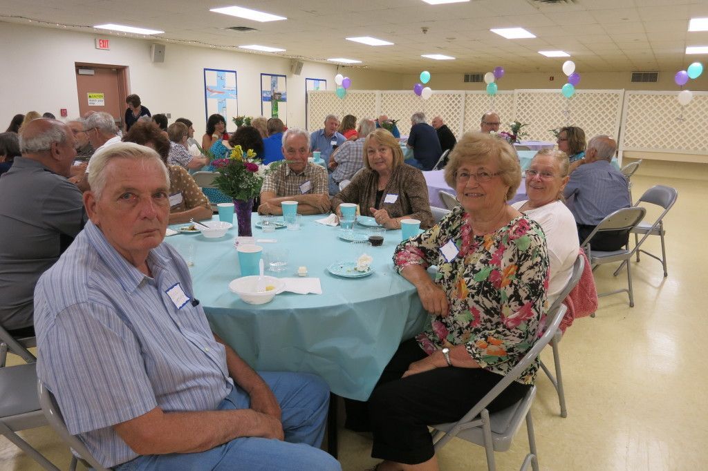 People seated at round tables in a bright community hall during a social gathering