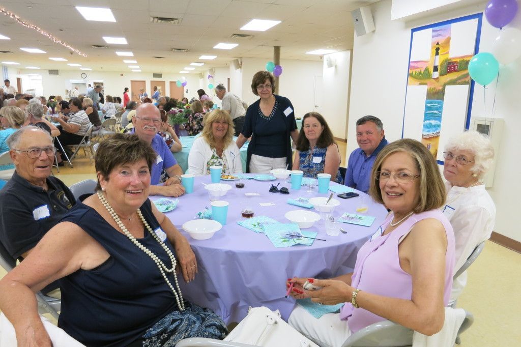 People seated around a round table at a lively indoor gathering, with purple tablecloths and balloons.