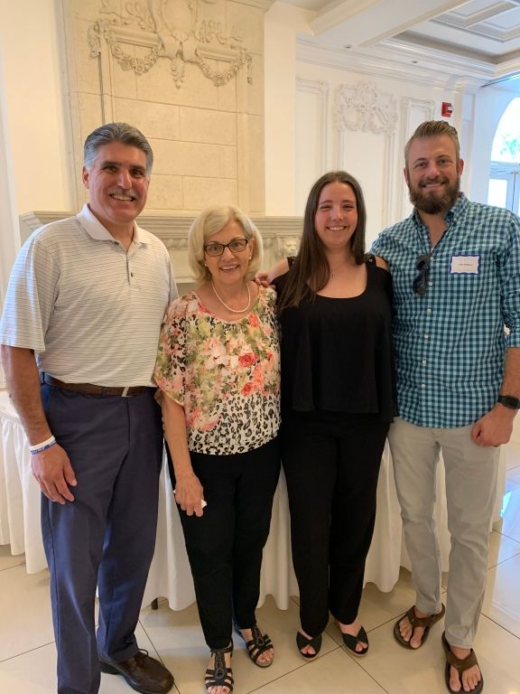 Four people smiling indoors in a bright ornate room, standing together for a group photo