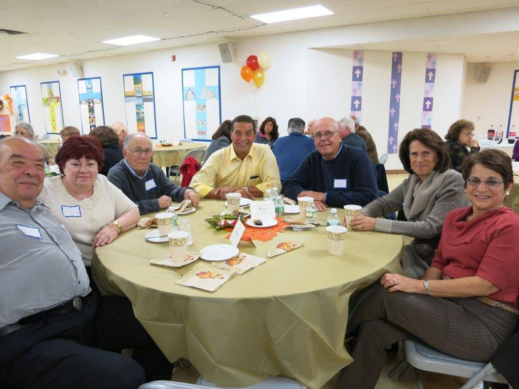 People seated around a banquet table in a bright community hall, sharing food and conversation.