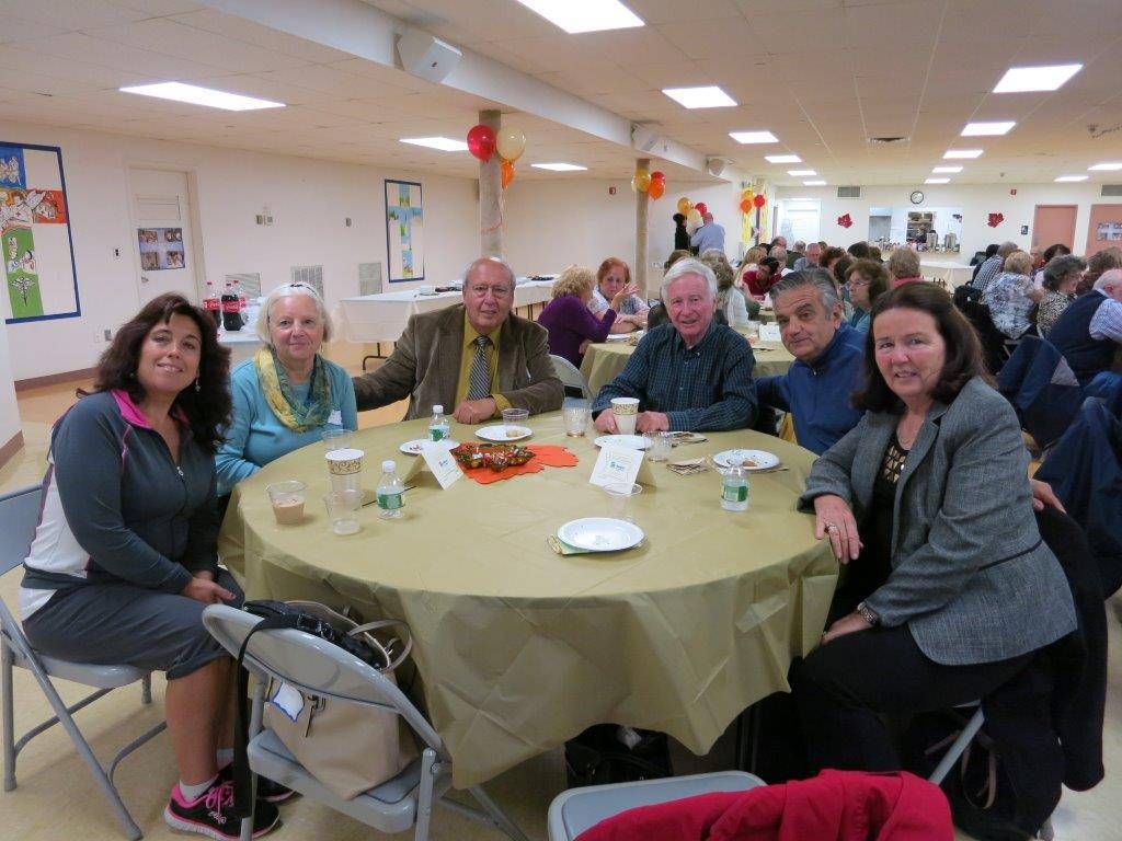 People seated around a table in a bright banquet hall, smiling at the camera.