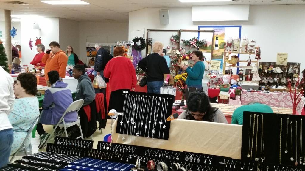 Indoor craft fair with people browsing tables of handmade items and gifts
