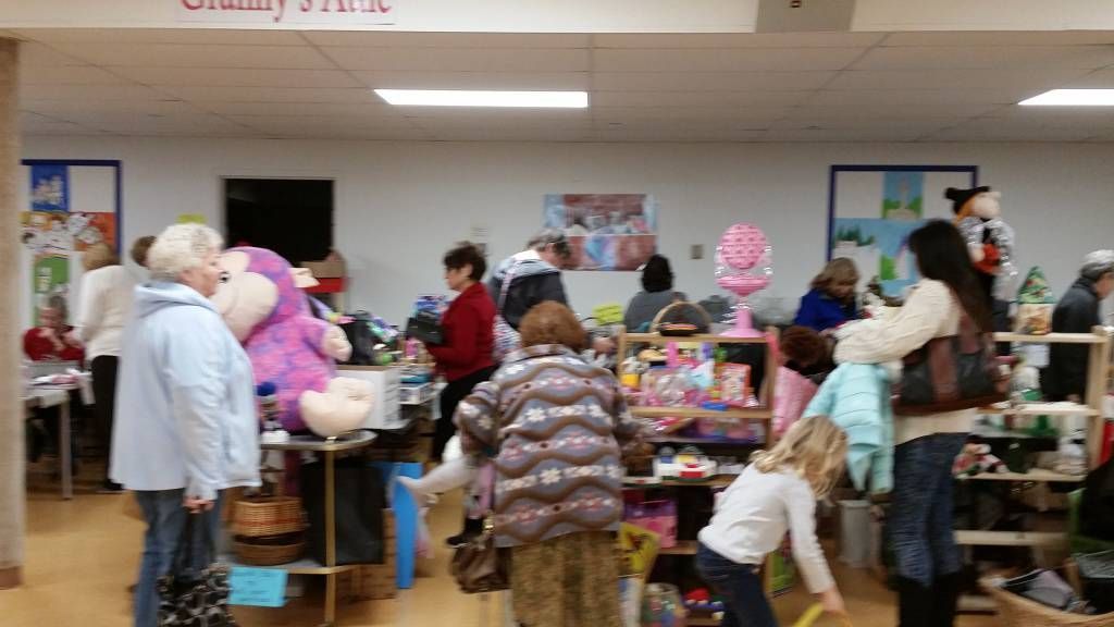 People browsing tables of stuffed animals and toys at a crowded indoor community sale
