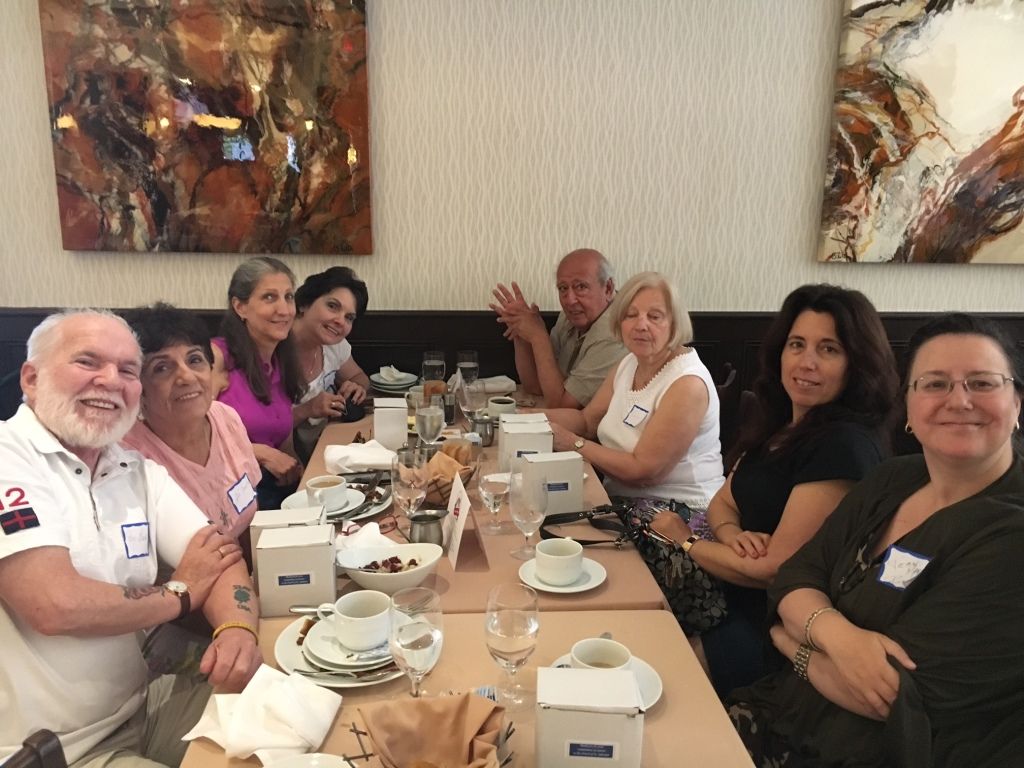 People seated around a long restaurant table, smiling and chatting over coffee and tea.