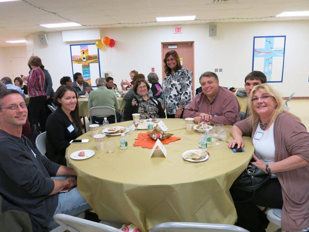 Group of people seated around a round table at a decorated indoor gathering, smiling at the camera.