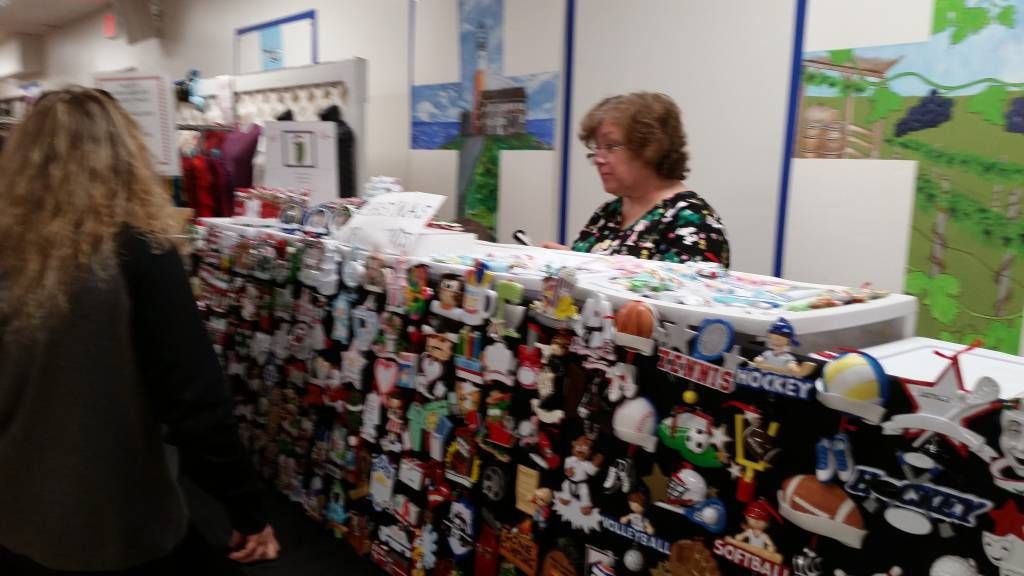 Vendor booth with a table covered in colorful handmade items, with two people browsing at an indoor fair.
