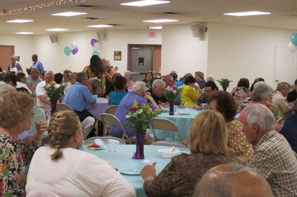 People seated at decorated banquet tables in a community hall, socializing over a meal.