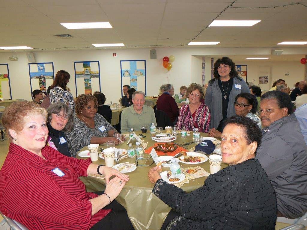 People seated at a banquet table in a community hall, sharing a meal and chatting.